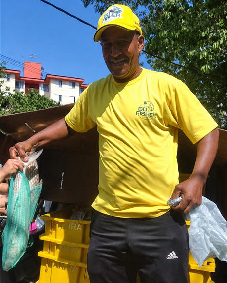 Voluntário de camisa amarela entrega um saco de peixe durante ação de distribuição.